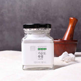 Bamboo salt jar with black lid and white salt powder beside a wooden mortar