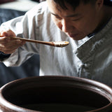 Ginger vinegar tasting with a spoon over a pot of dark liquid