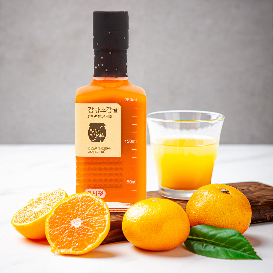 Fruit vinegar bottle with orange label, with glass of yellow vinegar and citrus fruit