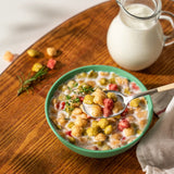 Bowl of creamy cereal with colorful puffs and spoon, with milk jug