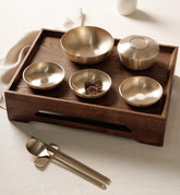 Single-person table set with wooden tray, five gold-tone metal bowls, and utensils