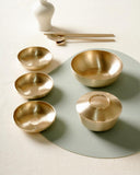 Single-person table set with five round metal bowls, utensils, and a small sauce bowl