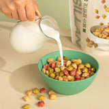 Milk being poured onto colorful cereal puffs in a green bowl