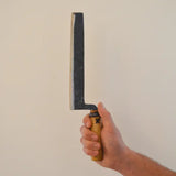 Bread knife held in hand, dark blade and wooden handle with metal ring at the bolster
