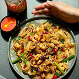 Plate of noodles with vegetables topped with chili crisp and chopped herbs