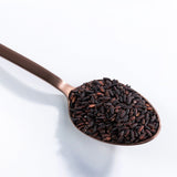 Organic germinated black rice grains in a metal spoon, dark black and brown