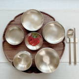 Single-person table set with round metal bowls, a wooden circular tray, and fork and spoon