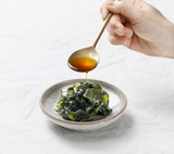Smoked fish sauce poured with spoon into bowl with leafy seaweed.