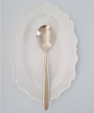 Metal serving spoon with oval bowl, placed on a scalloped white plate.