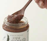 Spoon holding thick brown ssamjang paste above open jar.