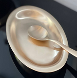Serving spoon in a shallow oval bowl, close-up with reflective finish.