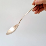 Long-handled metal serving spoon held by a hand above a smooth surface.