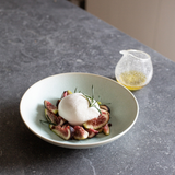 Cream-colored pasta bowl with topped food and herbs