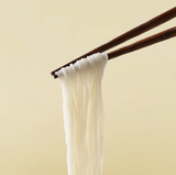 White thin rice noodles hanging from chopsticks, glossy strands