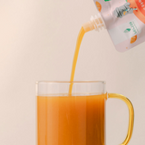 Tangerine juice being poured into a clear glass mug