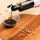 Soy sauce bottle pouring dark liquid into a glass bowl