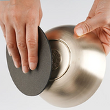 Dark abrasive sponge held against stainless steel bowl for cleaning