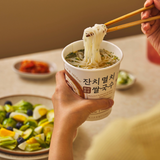 Hand holding rice cup noodles with chopsticks lifting strands from paper cup