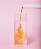 Glass with orange liquid being poured from a pink plum extract pouch