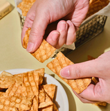 Hands holding fried fish chips pieces above a plate of golden snacks
