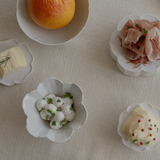 Small white flower-shaped bowls with scalloped edges, arranged with food