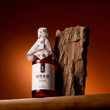 Smoked fish sauce bottle with wrapped cap and amber liquid, next to wooden piece.