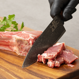 Chef knife slicing raw meat on a cutting board, dark Damascus blade, wood handle