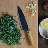 Chef's knife on a wooden board, dark blade with wooden handle.