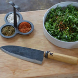 Chef's knife on a wooden board with dark blade and wooden handle.