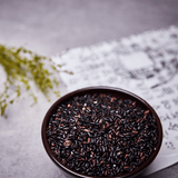 Bowl filled with black rice grains with a white bag behind