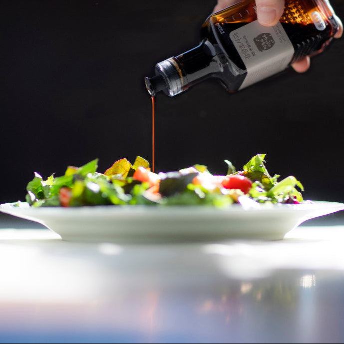 Fruit vinegar bottle pouring amber vinegar onto a salad dish