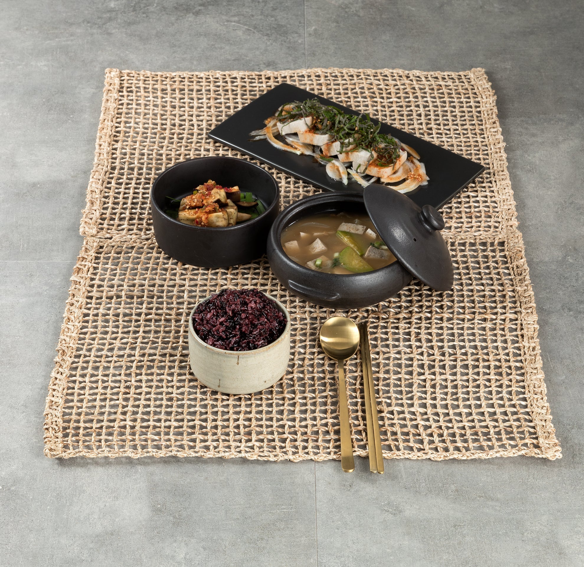Black germinated rice in a small bowl on a woven placemat with dishes