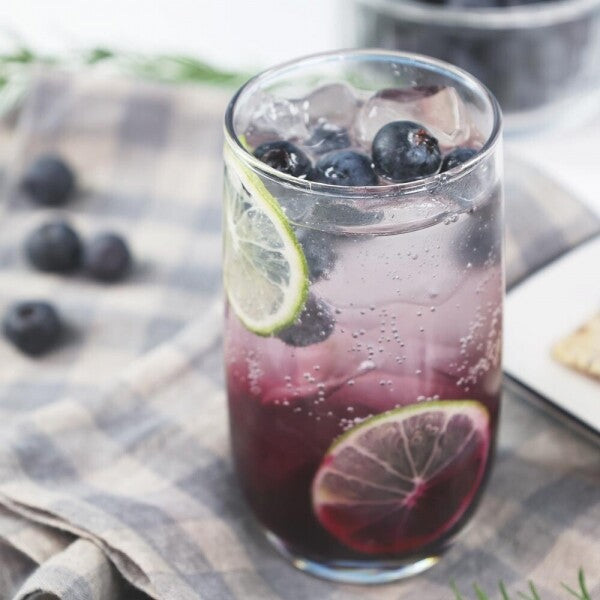 Blueberry jam beverage in a tall glass with ice and lime slice
