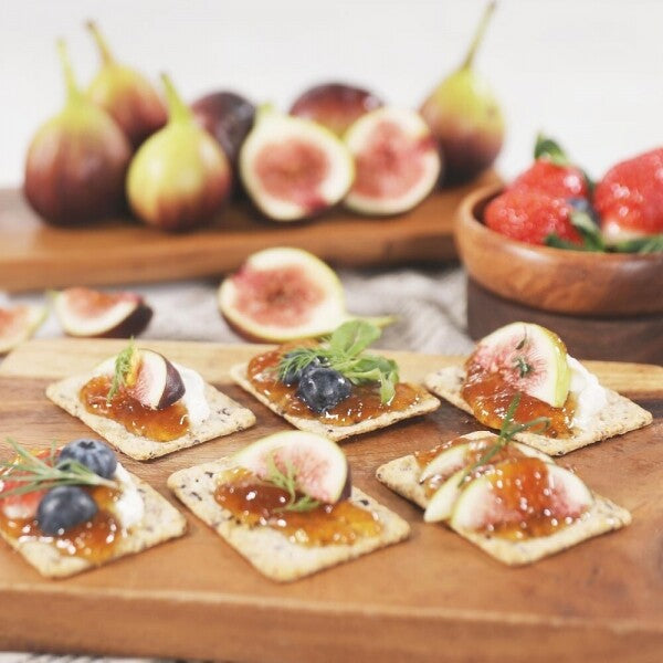 Jam-topped crackers on a wooden board with fruit around