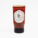 Syrup bottle with red-brown contents and white label, sealed cap and base.