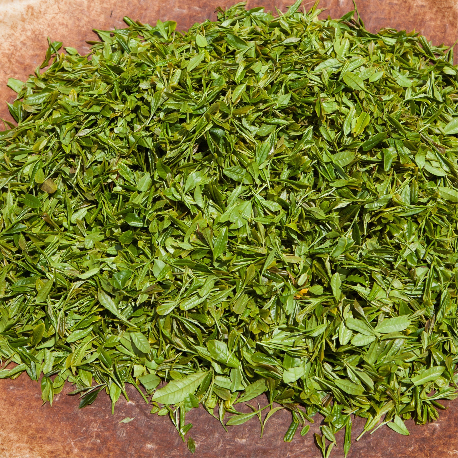 Pile of chopped green tea leaves spread on a brown surface