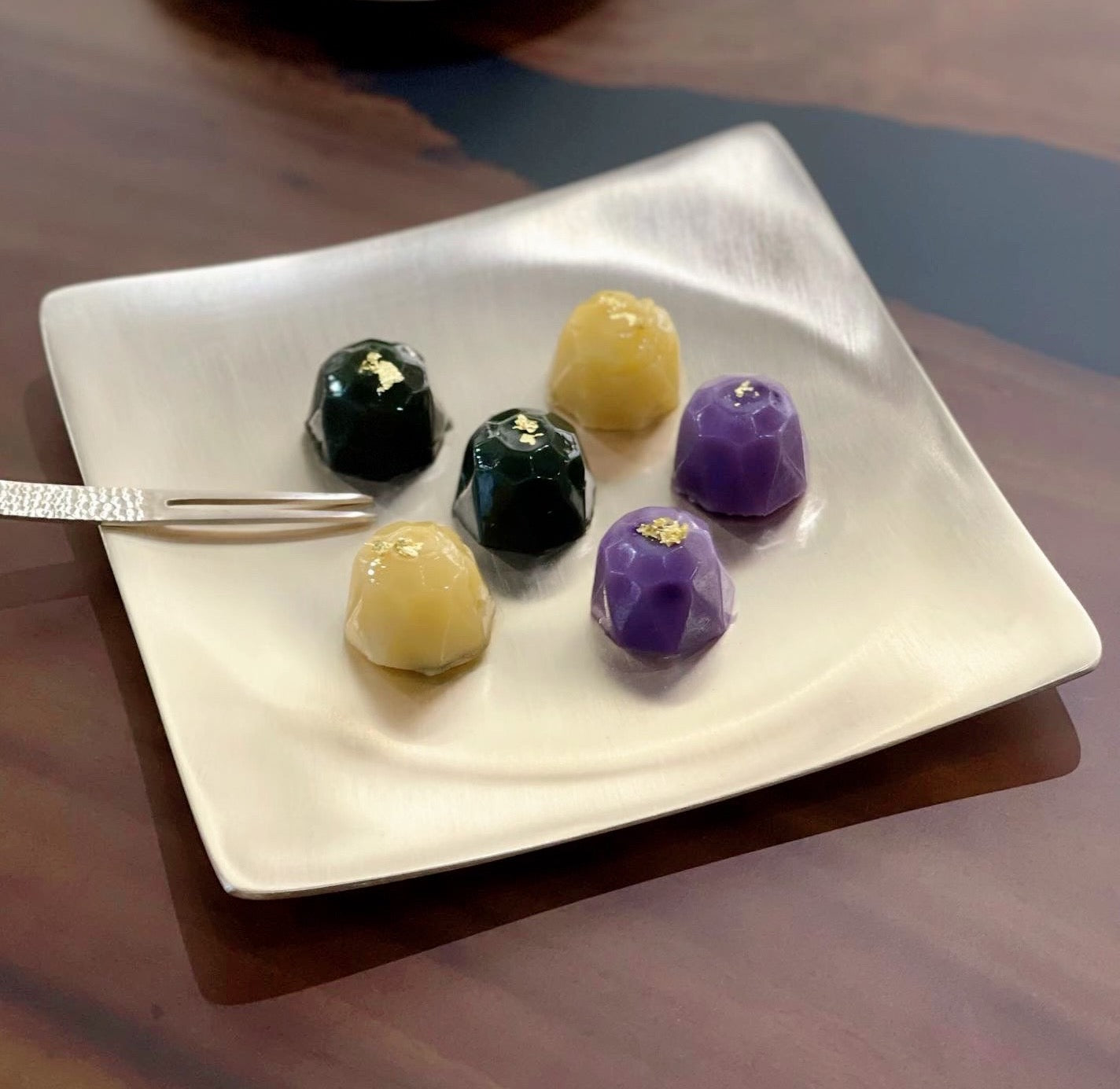 Bronze dessert forks with textured handles beside plated bite-size desserts