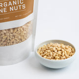 Organic Korean pine nuts in a white bowl beside a stand-up pouch
