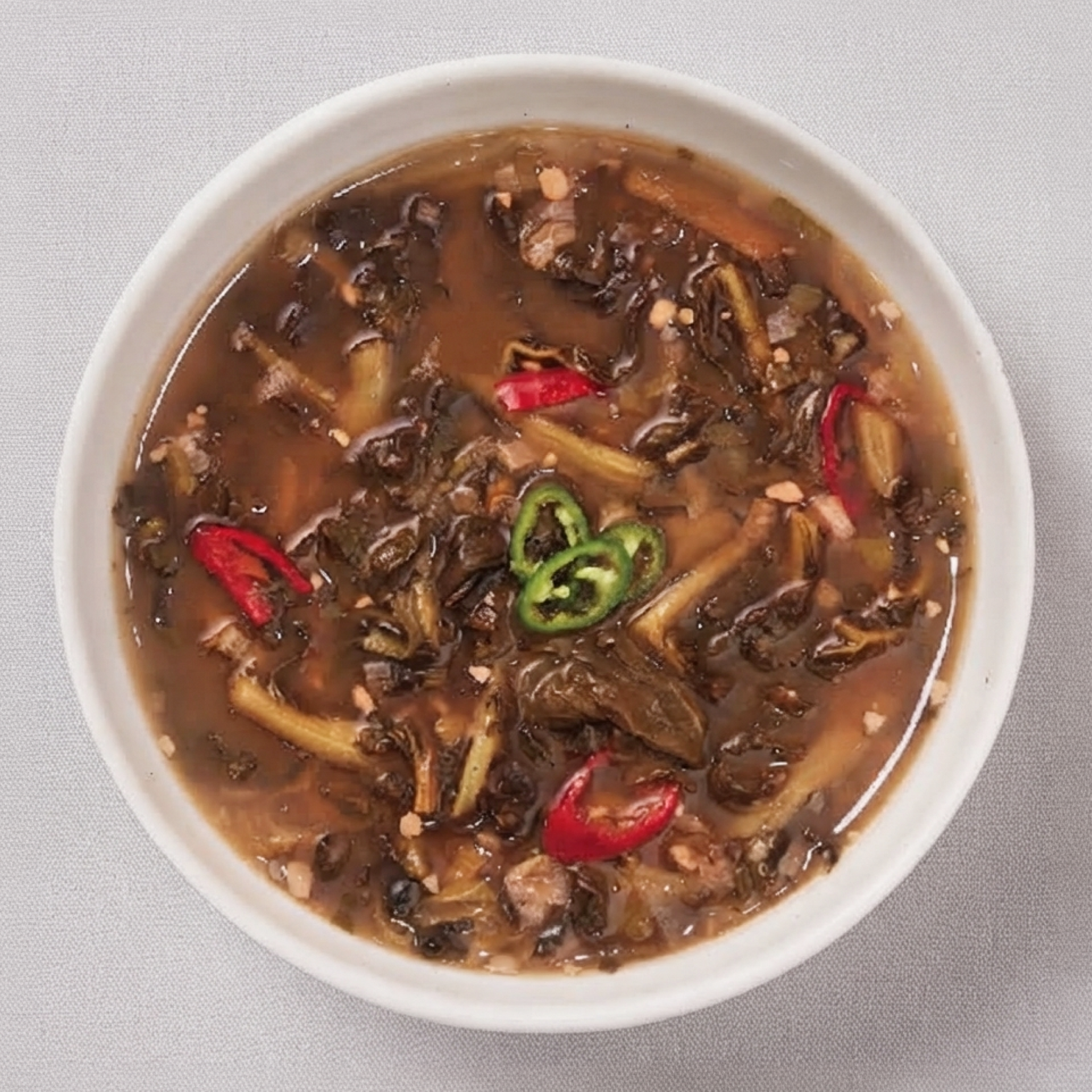 Spicy doenjang soup with dried radish leaves in a white bowl, red chili pieces