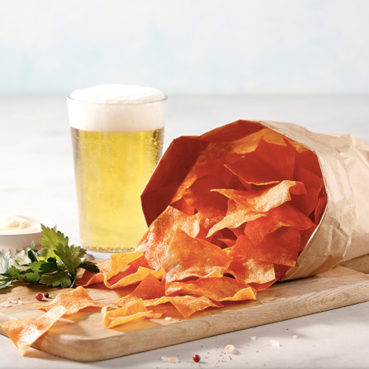 Paper-wrapped pile of crunchy orange kimchi chips on a wooden board