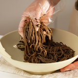 Lifted buckwheat noodles from a bowl with dark perilla oil and seasoning