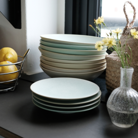 Stack of teal pasta bowls with a pale green serving bowl