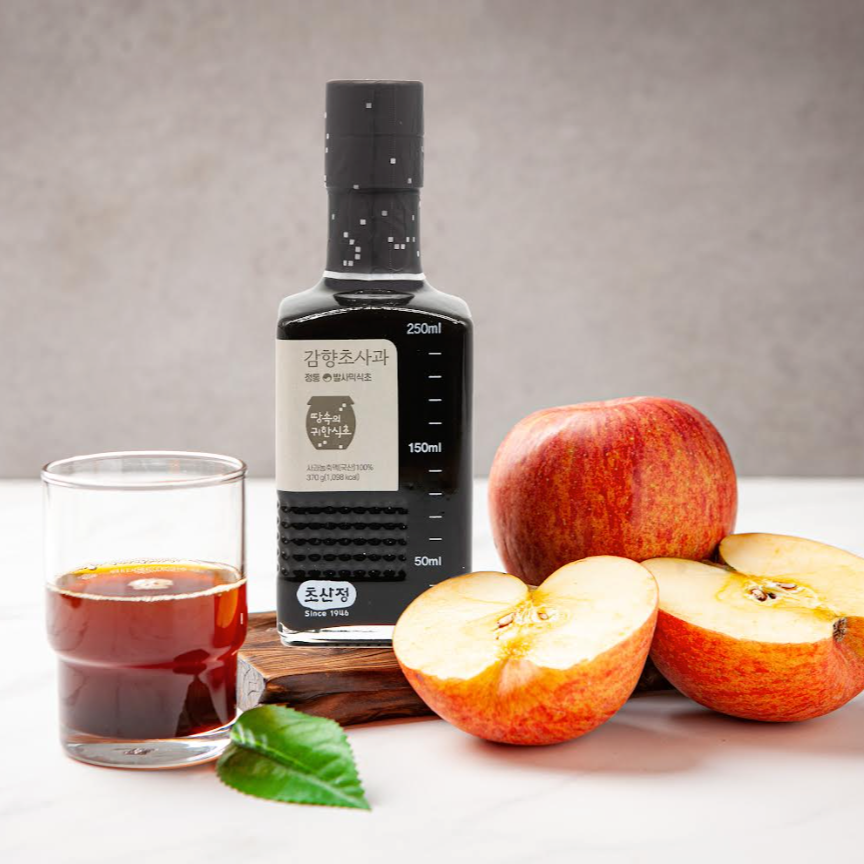 Fruit vinegar bottle with dark cap, beside glass of red vinegar and sliced fruit