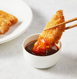 Tonkatsu sauce in a white dipping bowl with breaded cutlet on chopsticks