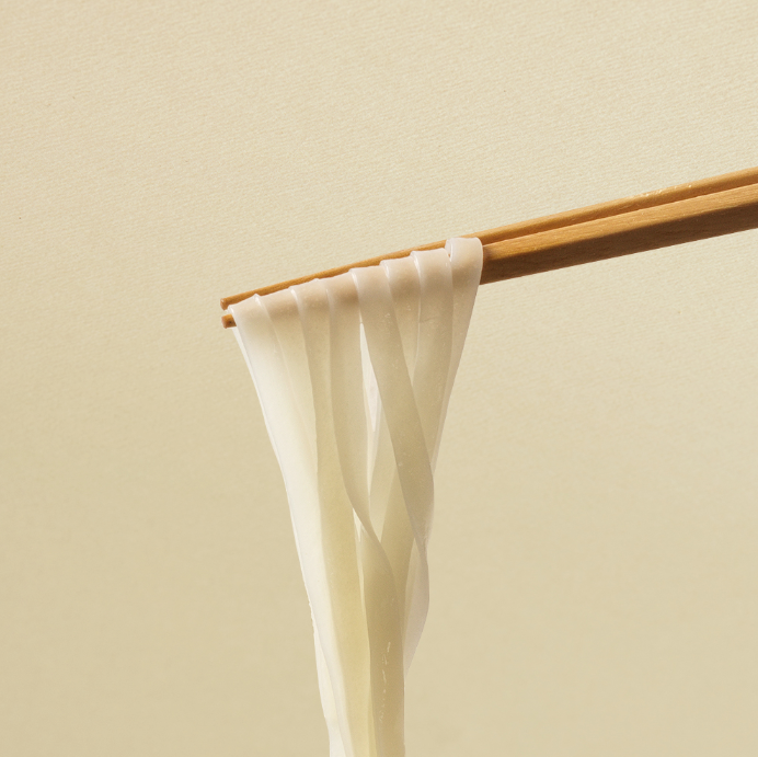 Flat rice noodles on chopsticks, pale uncooked sheets