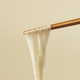 Flat rice noodles on chopsticks, pale uncooked sheets