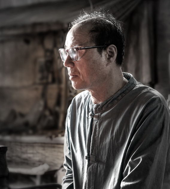 Chef in a workshop wearing a gray smock and glasses; no knife visible.