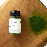 Powder jar with black lid beside mound of green powder on wood