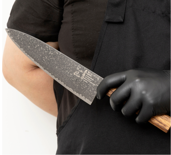 Chef knife held by gloved hand, speckled Damascus blade, wooden handle