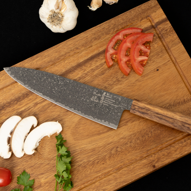 Damascus chef knife on wooden board, gray speckled blade with wood handle